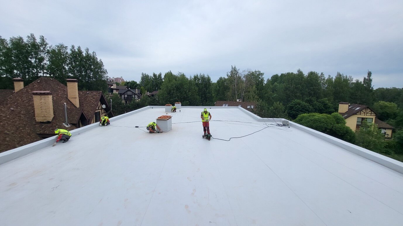 Сварка швов ПВХ-мембраны на плоской крыше, кровельщики в процессе монтажа