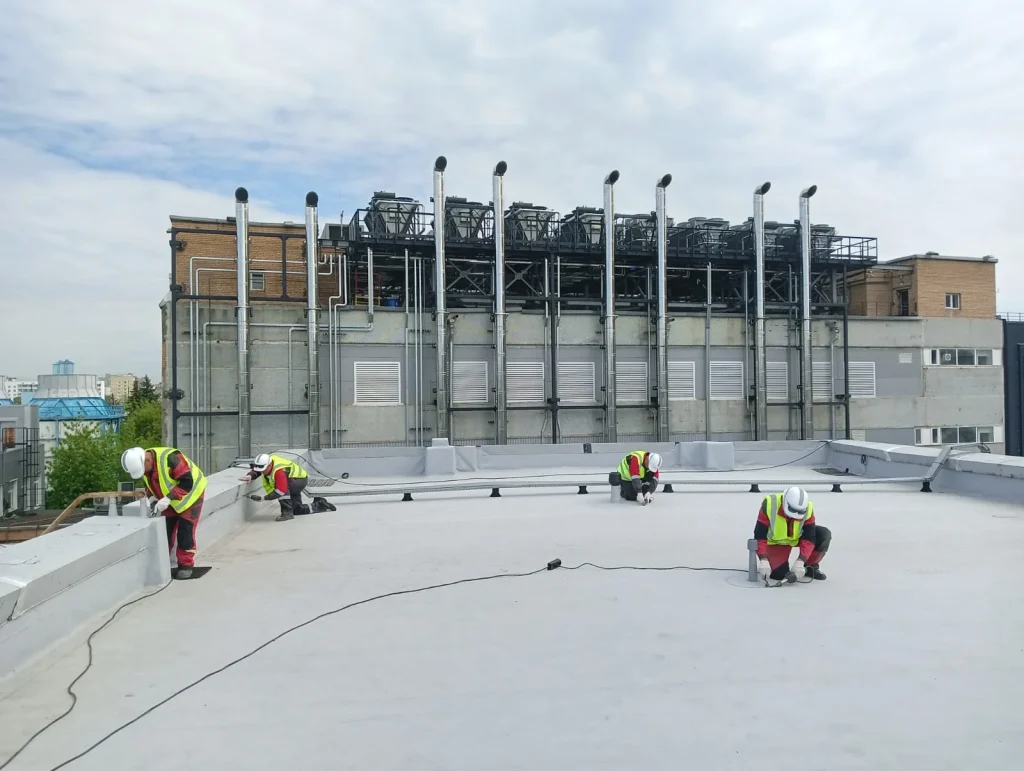 Ремонт плоской кровли на промышленном здании с инженерными коммуникациями на заднем плане
